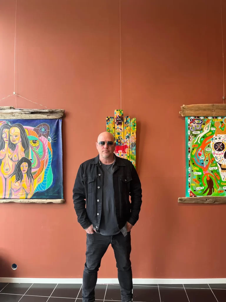 Fishbain standing in front of his paintings hanging on a wall at Gallery vinbar in Gamlebyen Fredrikstad